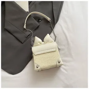 Detail view of cream woven mini crossbody bag featuring a chic bow and silver chain