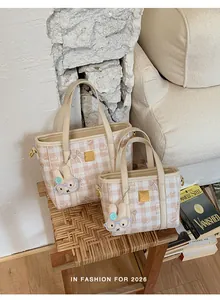 Detailed view of two checkered beige tote bags with cute bunny charms on a wooden stool.