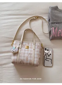 Close-up of a small beige plaid tote bag featuring a cute rabbit charm and shoulder strap