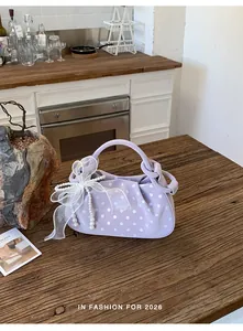 Lavender polka dot dumpling bag with elegant pearl ribbon bow detail on rustic wood table