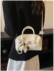 Cream patent leather Boston bag with a horse charm, worn cross-body over a black blazer.