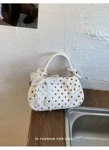 Detailed view of white polka dot dumpling bag featuring elegant mesh bow and pearl charms