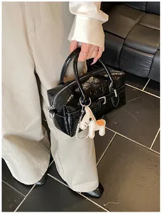 Detail shot of a high-end black patent leather Boston bag with a horse charm for women.