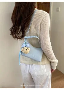 A chic light blue underarm shoulder bag with a bear charm shown worn by a model