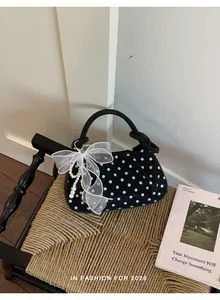 Detailed view of a black polka dot handbag featuring a white mesh bow and pearl charms