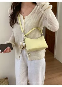 Pale yellow minimalist underarm bag worn crossbody with a cute teddy bear charm