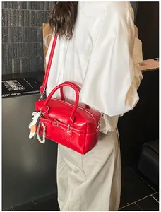 Detailed view of a chic red glossy Boston bag with a pearl and dog charm decoration.