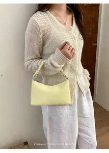 A detailed visual of a pale yellow minimalist leather underarm bag held by a model