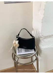 Minimalist chic black underarm bag with cute bear charm displayed on a stylish metal stool