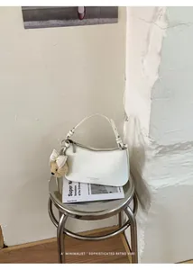 Sleek white minimalist leather underarm bag with a cute bear charm on a metal stool