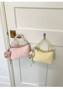 Pink and yellow minimalist hobo bags with cute bear charms hanging on a white door