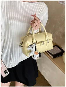 Close-up of stylish cream yellow Boston bag featuring a white horse charm and pearl chain