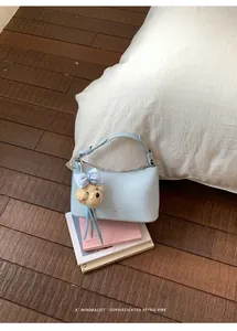 Close-up detail of a minimalist light blue hobo bag with a cute teddy bear charm