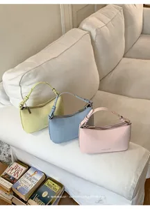 Detail shot of three minimalist pastel faux leather shoulder bags on a white sofa