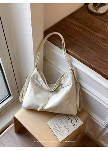 Dettaglio di una borsa tote color crema posata su uno sgabello in legno.