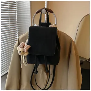Schwarzer minimalistischer Rucksack mit süßem Teddybär-Anhänger auf beigem Blazer.