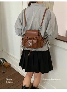 Detail view of stylish brown faux leather backpack with silver bow knot on model