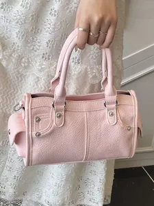 Elegant pink litchi grain leather handbag held by hand against white lace dress background