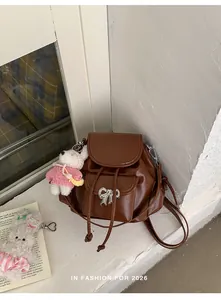 Chic brown mini backpack with silver bow and plushie charm in a lifestyle setting