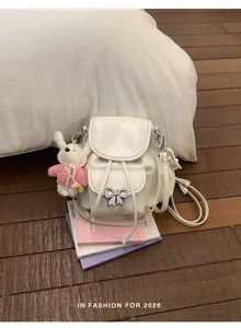 Detail view of a cream-colored sweet style backpack with silver bow and rabbit charm.