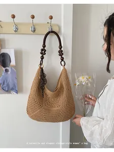 Vintage-style woven straw bag with wooden bead handle displayed on a wall hook