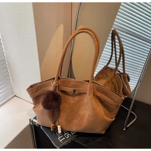 Detailed view of a vintage pleated suede tote bag with a decorative fur ball charm