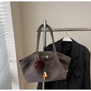 Detail view of a vintage pleated tote bag with a fur ball charm on a clothing rack