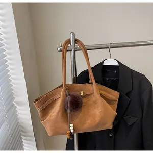 Detail of a vintage brown pleated tote bag hanging on a rack with a pompom charm.