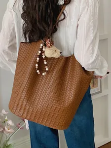 Fashionable brown woven tote bag for women featuring a plush bear charm and beads