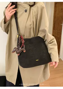 Detailansicht einer großen schwarzen Tragetasche mit Dackel-Anhänger an einem Trenchcoat
