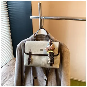 Detail shot of a vintage beige crossbody bag with a cute bear charm and brown trim.