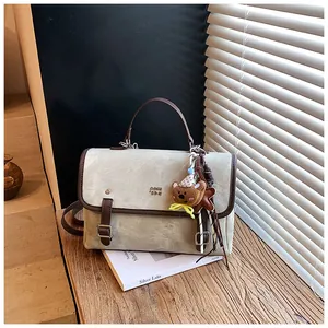 Elegant beige suede shoulder bag with brown trim and a cute teddy bear charm detail