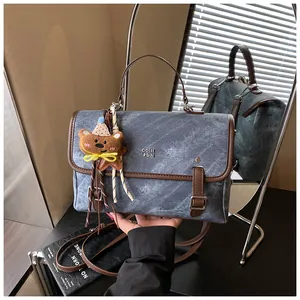 Chic blue denim textured handbag with brown trim and a cute plush bear charm detail.