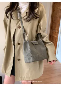 Detalle de un bolso tipo cubo gris minimalista combinado con una elegante gabardina beige.