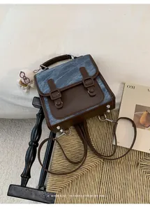 Zaino vintage in denim blu e pelle marrone esposto su una sedia intrecciata con decori