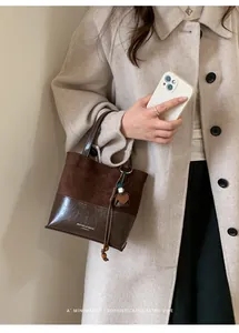 Detail view of a vintage brown suede and leather patchwork tote bag held by a model