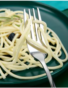 Close-up of a durable stainless steel fork winding spaghetti on a green plate.