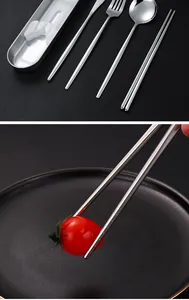 Close-up of portable stainless steel chopsticks picking up a cherry tomato on a plate