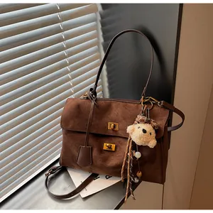 Close-up detail of a retro brown suede shoulder bag featuring a cute teddy bear charm