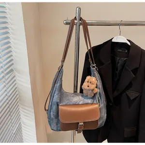 Detail of a blue denim shoulder bag with brown leather flap and cute bear charm.