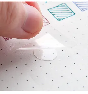 Close-up of a transparent circular double-sided adhesive dot being peeled for use
