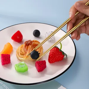 Elegant gold stainless steel chopsticks shown in use with colorful fruits on a plate.