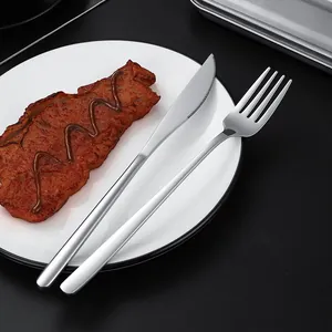 Sleek silver stainless steel knife and fork set on white plate with steak decoration