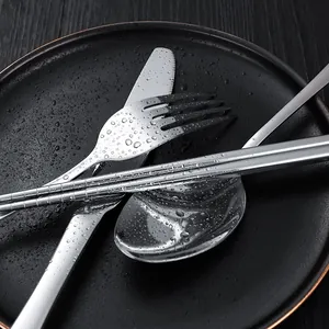 Modern stainless steel cutlery set including spoon fork and knife on black ceramic plate