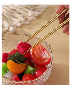 Close-up of golden stainless steel chopsticks picking fruit from a decorative bowl