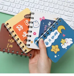Detailed view of hand holding cute A7 mini spiral notebooks with cartoon designs.
