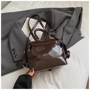 Detailansicht eines glänzend braunen Retro-Eimer-Rucksacks mit grauem Sakko kombiniert