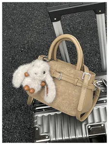 Khaki retro handbag with cute plush bunny charm resting on a silver suitcase detail