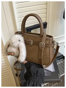 Detailed view of a brown matte handbag with a cute bunny charm on a silver suitcase