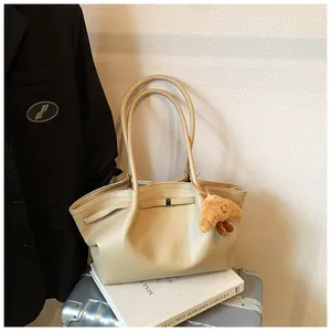 Elegante borsa tote in pelle martellata beige con charm a croissant su una valigia da viaggio